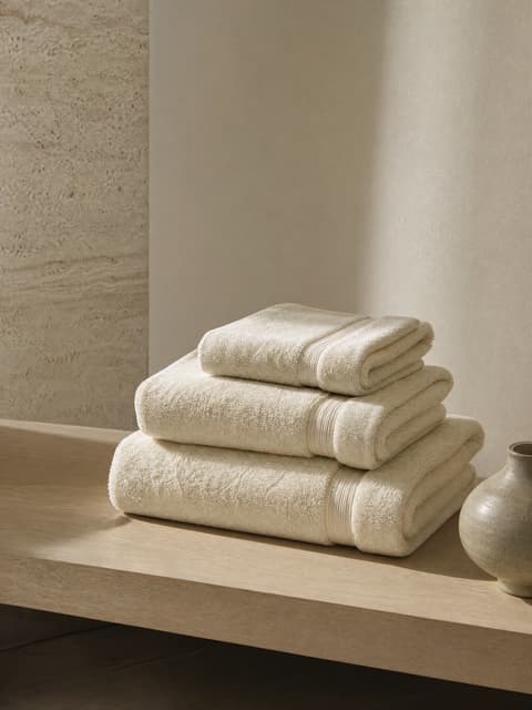 Freshly folded cream towels on a pale oak shelf