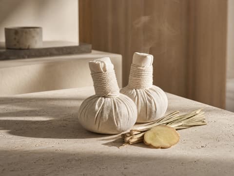 Two Thai herbal compresses with lemongrass and fresh ginger on pale stone